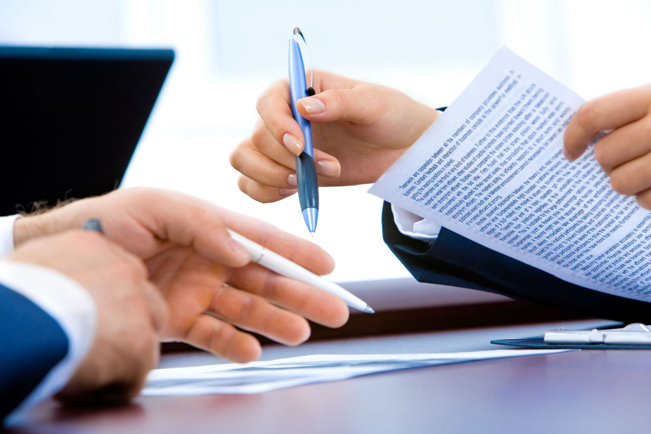 Manos intercambiando bolígrafos y documentos legales, simbolizando la firma de un acuerdo de divorcio.